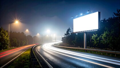 An illuminated blank billboard stands next to a winding highway at night, showing long exposure light trails from vehicles and a misty, foggy atmosphere.