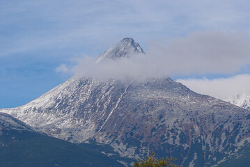Snowy peaks in the High Tatras rise above silent slopes. Thin clouds drift slowly across the sharp summit in a calm arc. Cold light glints on rugged ridges that stretch toward distant valleys.