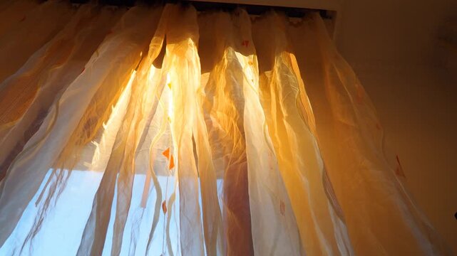 Warm sunset glow. Peaceful transition of daylight to dusk through the window, creating a serene atmosphere. The movement of sunrays can be seen on orange transparent curtains. Indoor interior