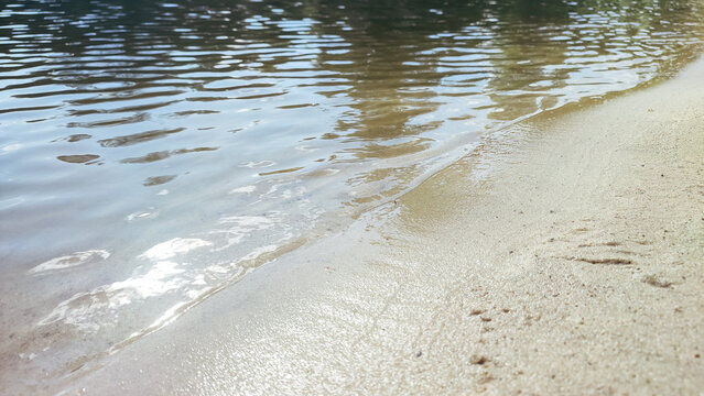 Reflection of clouds and sky in calm lake water with a sandy shore. - Powered by Adobe
