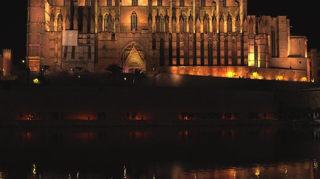 The majestic Cathedral of Santa Maria of Palma, known as La Seu, beautifully illuminated at night, with its impressive gothic architecture reflecting on the calm water of the Parc de la Mar