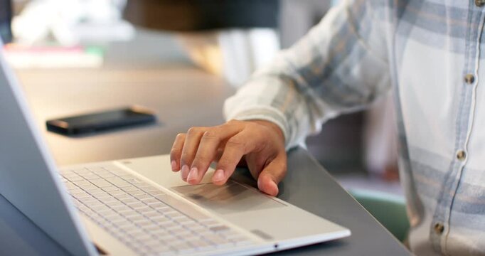 Camera focusing on right hand tapping trackpad causing male typing on laptop at desk, copy space