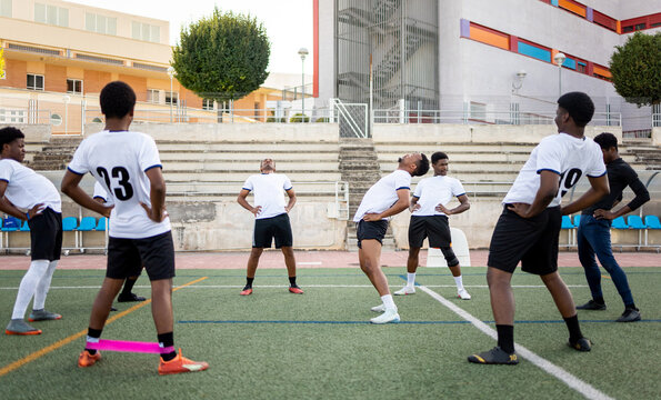 A group of dark-skinned soccer players are stretching their backs on a grass soccer field, wearing white uniforms. Grass soccer concept. African boys stretching before playing.