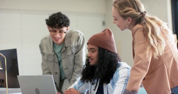 Diverse coworkers collaborating on laptop upon scrolling through document, revising draft in office