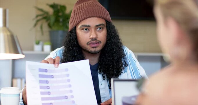 Diverse coworkers lifting printed horizontal bar chart at desk indicating data bars for discussion