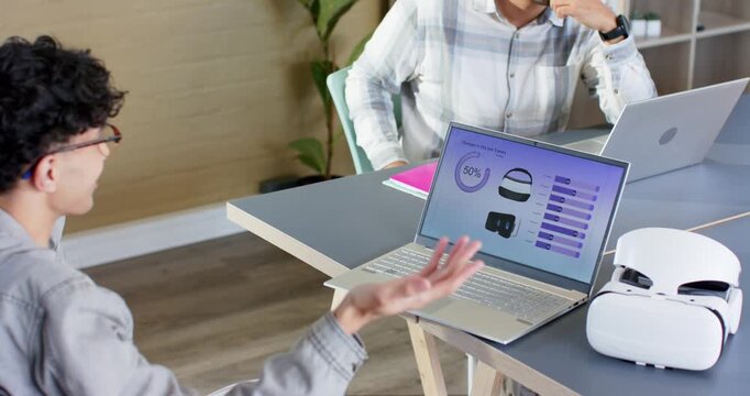 Diverse coworkers responding to VR stats slide, gesturing at laptop and typing notes at office