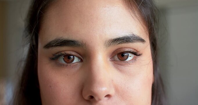 Female blinking at camera in front of pale wall, tightening brow and forming frown on forehead