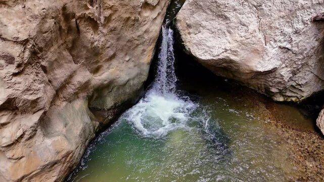 Mountain river cascading into a turquoise pool, surrounded by steep rocky cliffs, creates a pristine landscape in a remote gorge