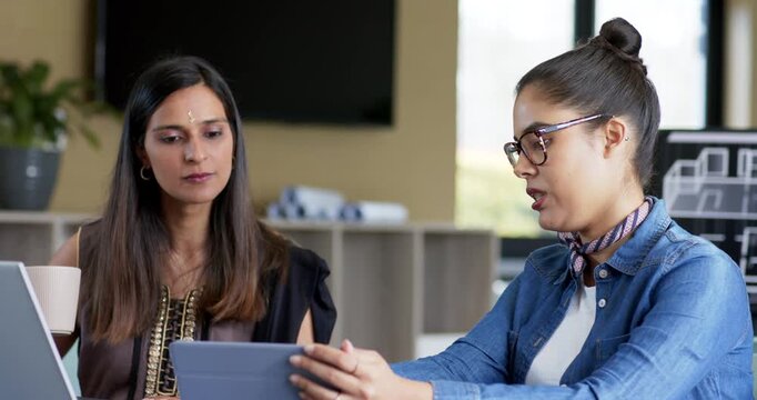 Reaching for tablet starting discussion Diverse female colleagues discussing ideas at office table