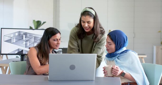 Diverse female coworkers working at laptop with mugs after lead presenting 3D floorplan on monitor