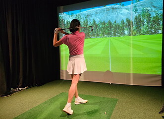 Woman practicing her golf swing indoors with a virtual golf simulator