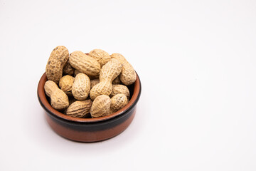 Monkey nuts in small earthenware dish on plain background