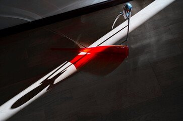 Still life with a red glass bottle and a juicer in a narrow beam of sunlight on a dark background.
