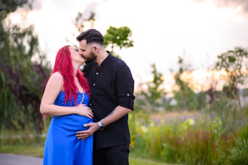 A couple kisses during a walk, the man gently holding the pregnant woman&rsquo;s belly. A warm moment of love and expecting a baby, surrounded by nature and soft evening light