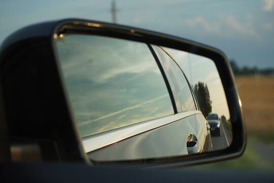 Side mirror view of a car driving on a road at sunset