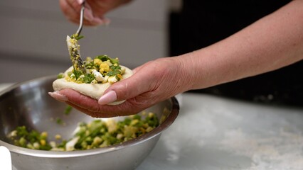 Hands filling dough with egg and herb mixture