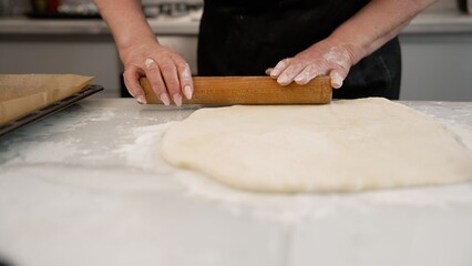 Hands rolling dough on a floured kitchen counter