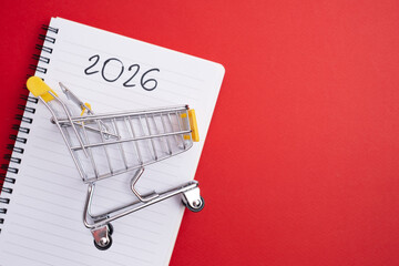 2026 Budgeting strategy. Miniature shopping cart and notebook for financial planning