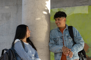 Diverse college students smiling and conversing outdoors on campus during a study break. Wearing casual clothing and carrying backpacks. Symbolizing friendship. Education