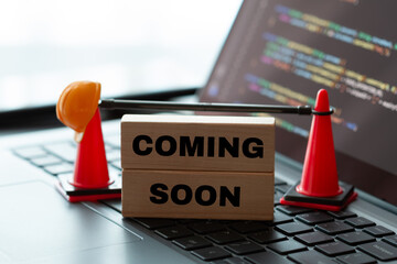 Engineer's hard hat, cone, and a "Coming Soon" sign on a laptop showing code, symbolizing system maintenance and upgrades