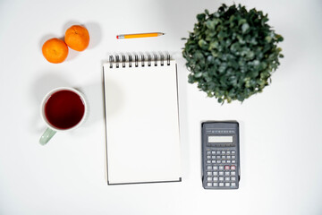 Flat lay of a blank notepad, calculator, tangerines, and tea. Ideal mockup for financial budgeting, diet planning, or healthy lifestyle resolutions.