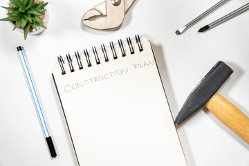 "Construction Plan" handwritten on a notepad surrounded by a hammer, wrench, and screwdrivers. Concept of home renovation, DIY, and contractor work.