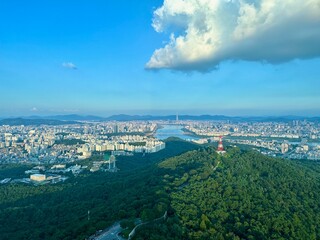 Panoramic View of a Lush Green Hill Overlooking a Bustling Cityscape with a River and Blue Sky with Clouds