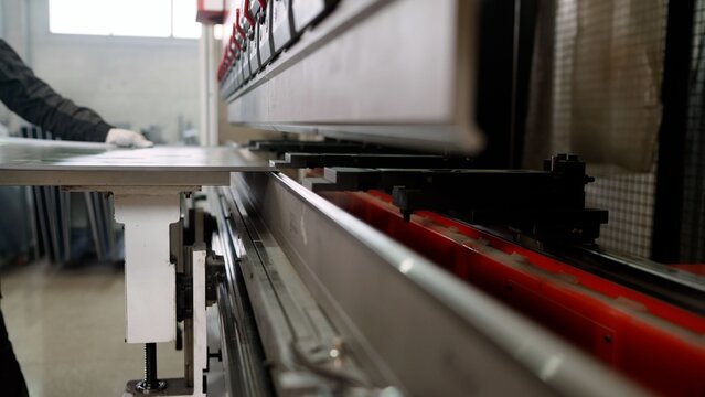 Close-up of an automated hydraulic press brake bending a metal sheet. An industrial worker is operating the machinery in a factory
