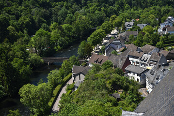 Fototapeta premium Scenic view frome above of small European town surrounded by lush green forest and a river. Traditional houses, stone bridge and peacaful nature landscape. Concept of travel, tourism, countryside 