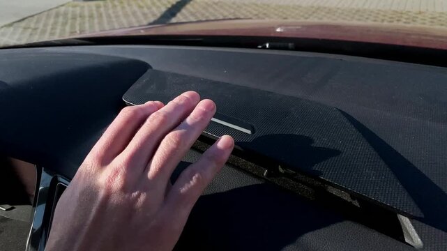 Opening small dashboard compartment near windshield in car interior with hand accessing slot designed for automatic gate or key-triggered access devices