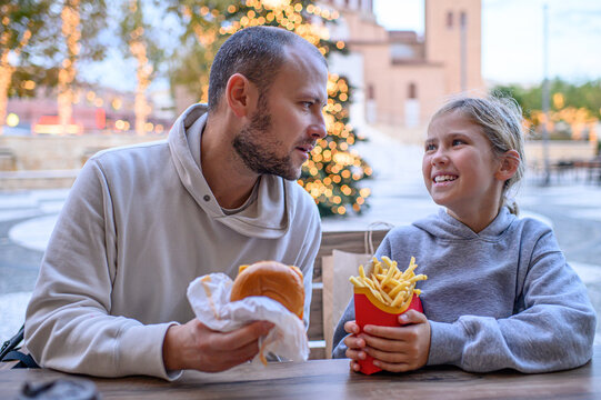 Father and daughter eating fast food in a shopping mall food court, enjoying a casual meal together and sharing a warm family moment indoors.