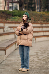Fototapeta premium Young woman holding small poodle dog outdoors in autumn park, showing pet care, companionship and everyday lifestyle.