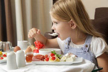 Cute little girl having breakfast, cereals with yogurt, tasty and healthy choice between various dishes served on the table	