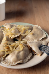 A plate of homemade polish dumplings topped with caramelized onions, with one piece cut open to reveal the filling. white mug in the background
