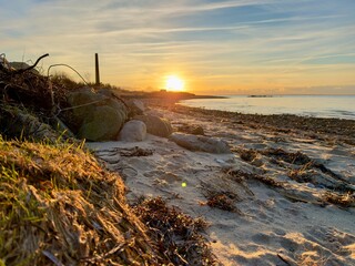 Sonnenuntergang an der Küste, am Strand von Dänemark mit Felsen und Seetank im Vordergrund