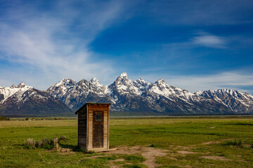 The snow covered Grand Teton Mountains with Mormon outhouse made of wood, landscape orientation.