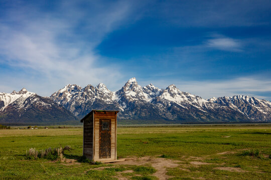 The snow covered Grand Teton Mountains with Mormon outhouse made of wood, landscape orientation.