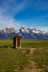 The snow covered Grand Teton Mountains with Mormon outhouse made of wood, portrait orientation.