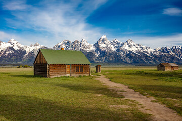 Obraz premium The snow covered Grand Teton Mountains in the background with a Mormon homestead and outhouse in Wyoming.