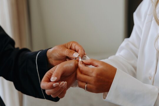 Close-up of two women's hands fastening a delicate bracelet on a wrist during wedding morning preparations