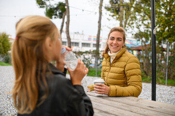 Mother and daughter enjoying coffee at an outdoor café, sitting together at a street table, sharing a warm moment in a relaxed urban atmosphere.