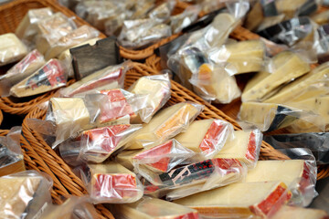 Assorted cheese varieties wrapped in clear plastic, displayed in woven baskets at a market, showcasing the rich textures and colors of gourmet dairy products