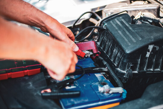 Under the hood of the car, the mechanic connects the clamp of the car jump starter to the terminal of the dead car battery