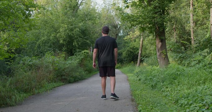 A man walks along path in green spring forest, limping on one leg