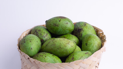 Raw green mangoes in a bamboo woven basket on a white background with ample negative space. Concepts: healthy tropical fruit, organic food, harvest, agriculture, and market produce.
