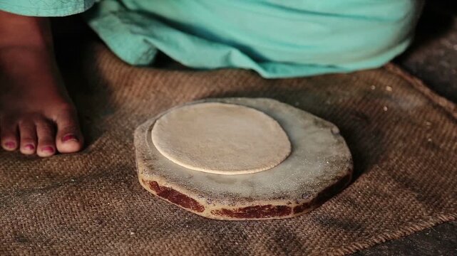 Close-up view of a village woman rolling freshly prepared dough on a traditional stone chakla, capturing the authentic process of making homemade roti in a rural Indian home.