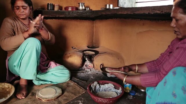A poor indian woman in traditional Indian attire kneads dough beside a clay oven, preparing flatbreads in a cozy, rustic kitchen. Simple utensils, a wood-fired stove, and everyday family life set the 