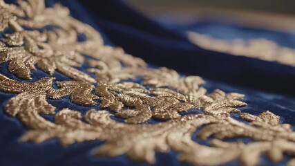 Close-up of gold embroidery on blue velvet fabric with detailed floral pattern and soft lighting - Powered by Adobe