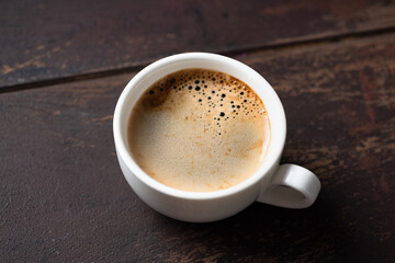 Fragrant cup of black coffee with beautiful coffee foam (crema) in white porcelain cup on old wooden table background