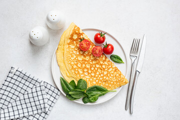 Delicious and healthy breakfast: folded omelette with baby spinach and cherry tomatoes on white plate, table top view food photo. Diet meal